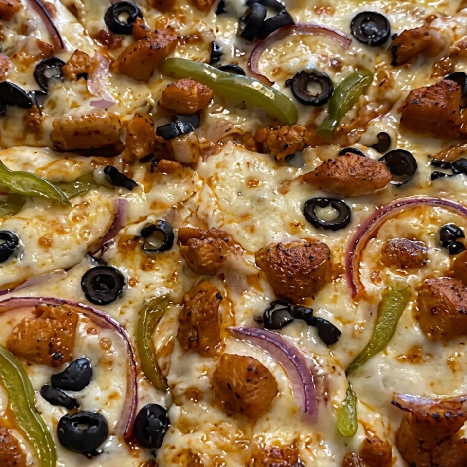 Close-up of a cheesy pizza topped with roasted chicken, black olives, green peppers, red onions, and tomato slices.